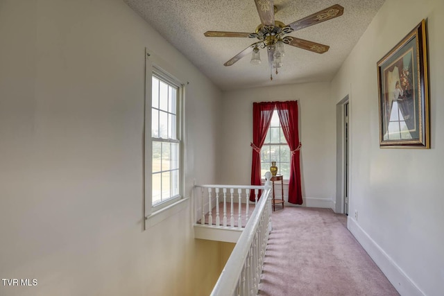 hall with light colored carpet, a textured ceiling, an upstairs landing, and baseboards