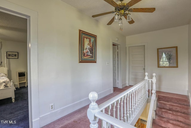hall featuring carpet floors, baseboards, a textured ceiling, and an upstairs landing