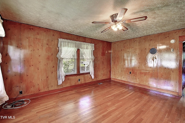 spare room featuring a textured ceiling, a ceiling fan, wood walls, and wood finished floors