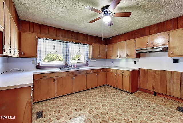 kitchen with ceiling fan, a sink, light countertops, a textured ceiling, and under cabinet range hood