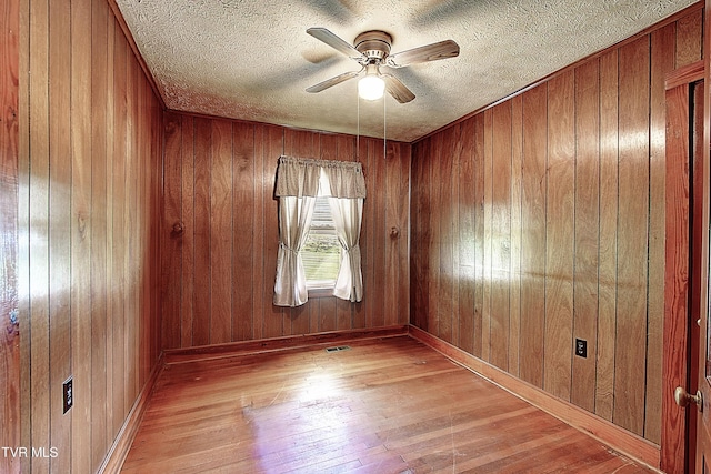 unfurnished room with a textured ceiling, ceiling fan, wood walls, and wood finished floors