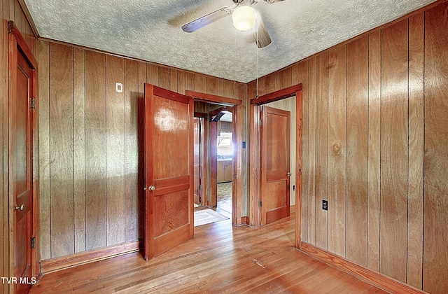 hall featuring wooden walls, a textured ceiling, and light wood finished floors
