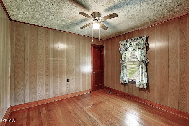 empty room with wooden walls, ceiling fan, wood finished floors, and visible vents