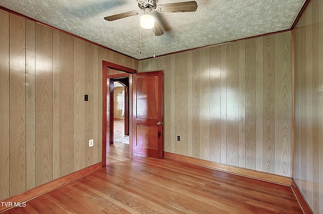 spare room featuring wooden walls, a textured ceiling, ceiling fan, and wood finished floors