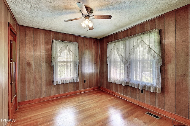 unfurnished room with ceiling fan, visible vents, wood walls, and wood finished floors