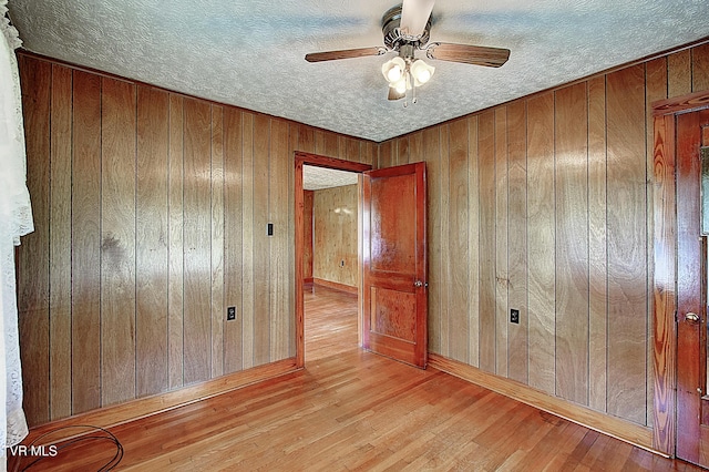 empty room featuring ceiling fan, a textured ceiling, wood walls, baseboards, and wood finished floors
