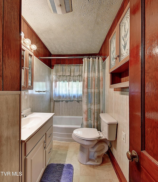 bathroom featuring wooden walls, vanity, shower / tub combo with curtain, toilet, and a textured ceiling
