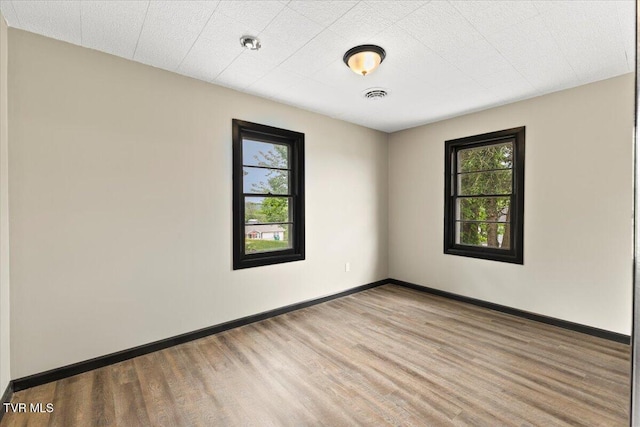 empty room featuring baseboards, visible vents, a wealth of natural light, and wood finished floors