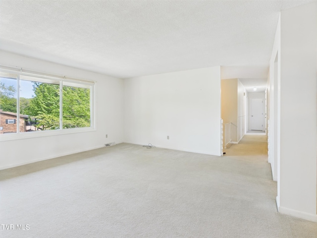 empty room featuring a textured ceiling, light colored carpet, and baseboards