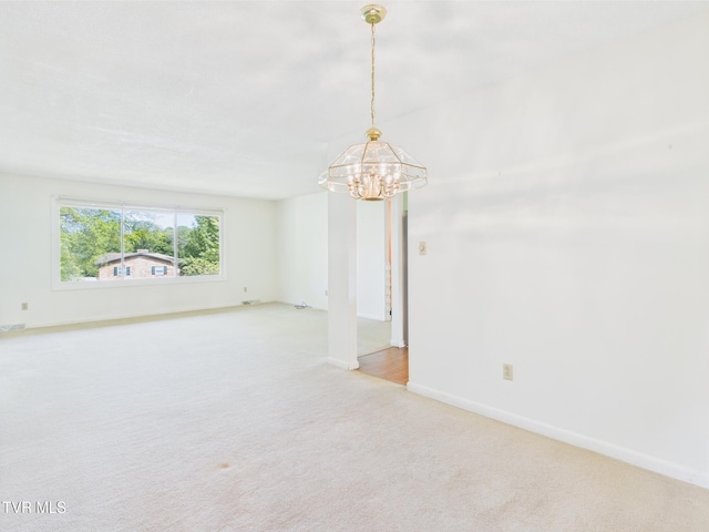 carpeted empty room with baseboards and a chandelier