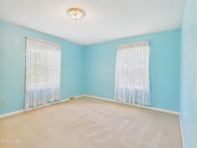 carpeted spare room featuring visible vents, a textured ceiling, and baseboards