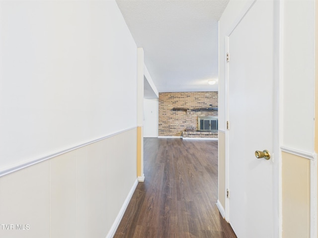 hall with a wainscoted wall, baseboards, dark wood-style flooring, and brick wall