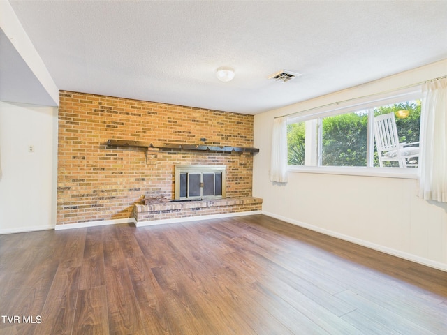 unfurnished living room with baseboards, a brick fireplace, wood finished floors, and visible vents