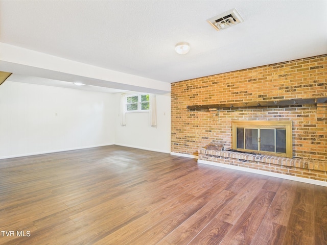 unfurnished living room with visible vents, baseboards, a brick fireplace, and wood finished floors