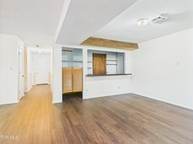 unfurnished living room featuring baseboards, a textured ceiling, visible vents, and wood finished floors