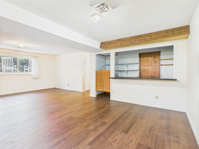 unfurnished living room with baseboards, a textured ceiling, visible vents, and wood finished floors