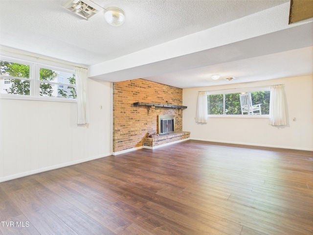 unfurnished living room featuring a fireplace, a textured ceiling, baseboards, wood finished floors, and visible vents