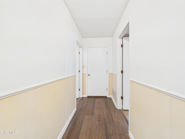 hall featuring visible vents, a textured ceiling, wood finished floors, and a wainscoted wall