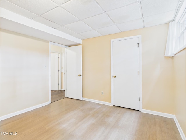 empty room featuring baseboards, a drop ceiling, and light wood-style floors