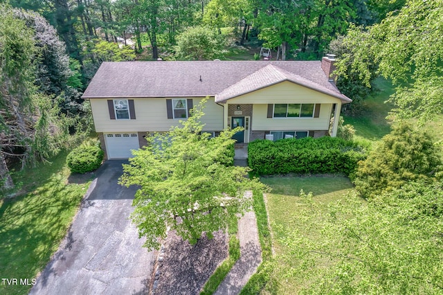 split foyer home with brick siding, an attached garage, a chimney, and aphalt driveway