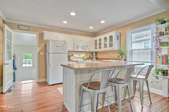 kitchen with crown molding, a breakfast bar area, white appliances, and a textured ceiling
