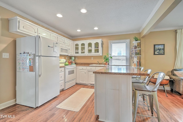 kitchen featuring crown molding, a breakfast bar, white appliances, light wood-style floors, and glass insert cabinets