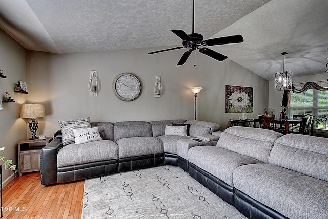 living area featuring a textured ceiling, vaulted ceiling, light wood finished floors, and ceiling fan with notable chandelier