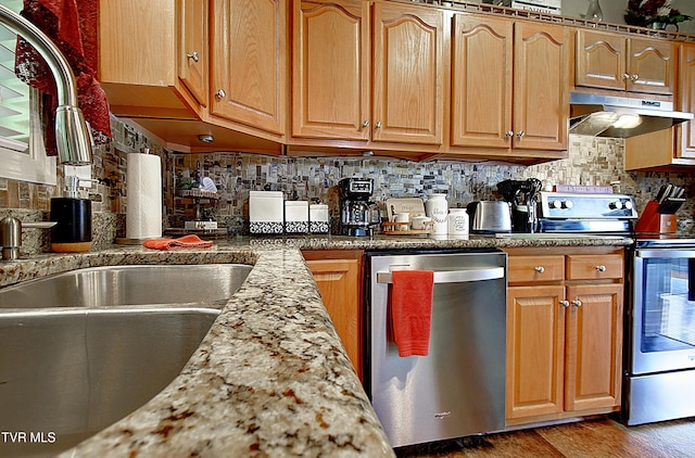 kitchen featuring under cabinet range hood, appliances with stainless steel finishes, decorative backsplash, and wood finished floors