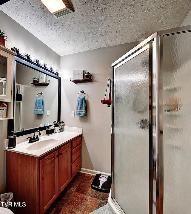 bathroom featuring stone finish floor, a textured ceiling, a stall shower, vanity, and baseboards