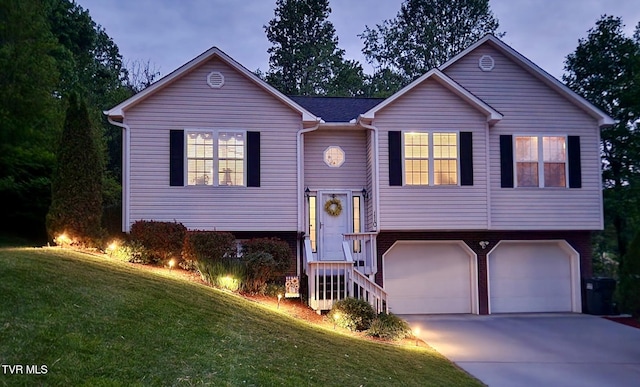 raised ranch featuring concrete driveway, an attached garage, and a front lawn