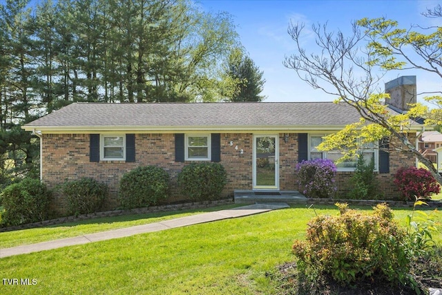 view of front of house featuring brick siding, a chimney, a front yard, and roof with shingles