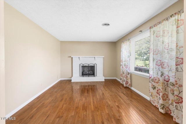 unfurnished living room with a textured ceiling, visible vents, a fireplace, wood finished floors, and baseboards