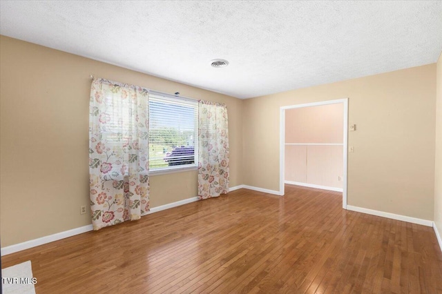 empty room featuring visible vents, a textured ceiling, baseboards, and hardwood / wood-style flooring