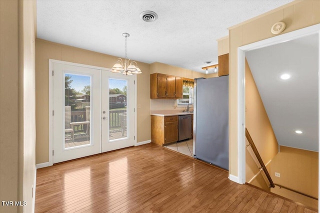 kitchen featuring a notable chandelier, appliances with stainless steel finishes, light countertops, brown cabinetry, and light wood-type flooring