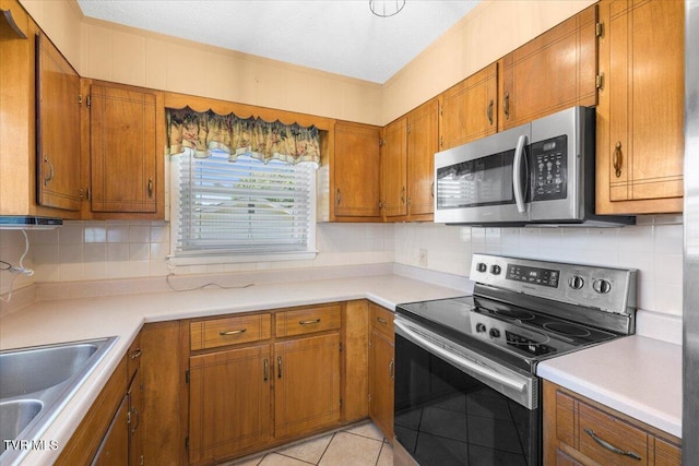kitchen with light countertops, brown cabinets, tasteful backsplash, a sink, and appliances with stainless steel finishes