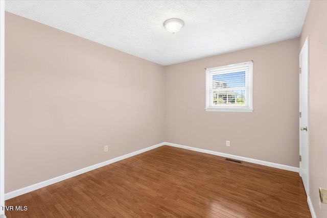 unfurnished room featuring a textured ceiling, baseboards, visible vents, and wood finished floors