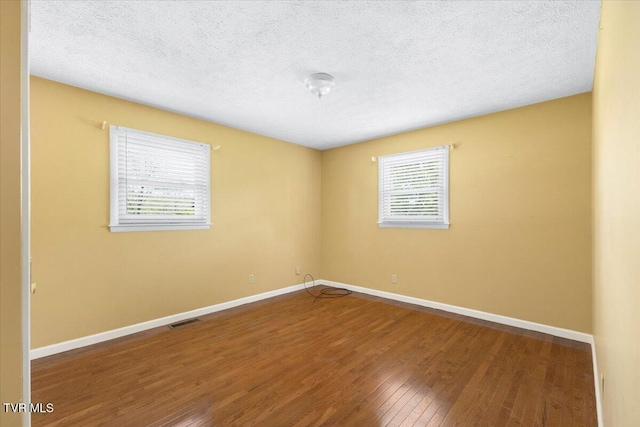 unfurnished room featuring a textured ceiling, baseboards, visible vents, and wood finished floors