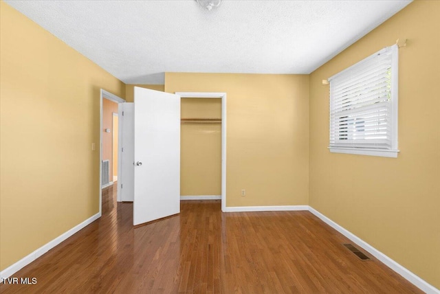 unfurnished bedroom with baseboards, visible vents, wood finished floors, and a closet