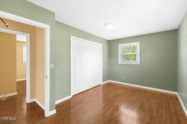 unfurnished bedroom featuring baseboards, wood finished floors, and a closet