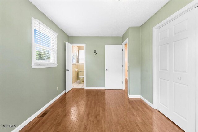 unfurnished bedroom with baseboards, ensuite bathroom, wood finished floors, and visible vents