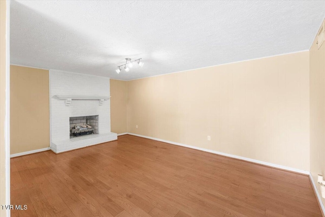 unfurnished living room with baseboards, a textured ceiling, a brick fireplace, and wood finished floors