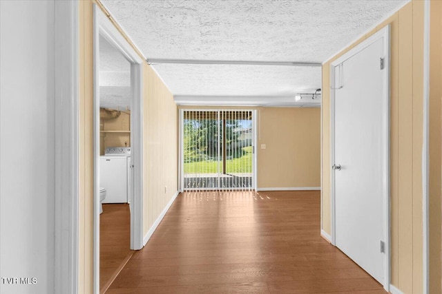 hallway featuring baseboards, independent washer and dryer, a textured ceiling, and wood finished floors