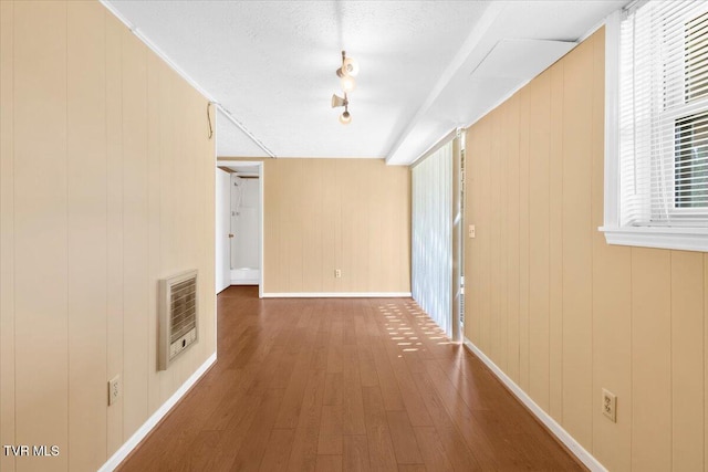 corridor with heating unit, baseboards, plenty of natural light, and wood-type flooring