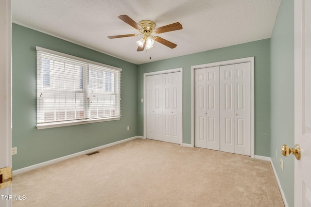 unfurnished bedroom with carpet flooring, a textured ceiling, baseboards, and multiple closets