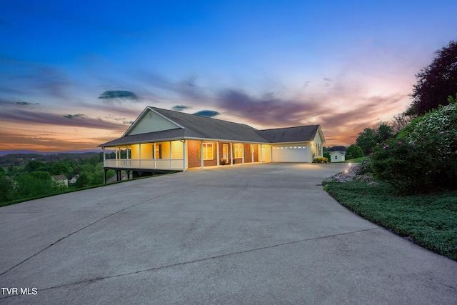 farmhouse-style home featuring covered porch, brick siding, an attached garage, and driveway
