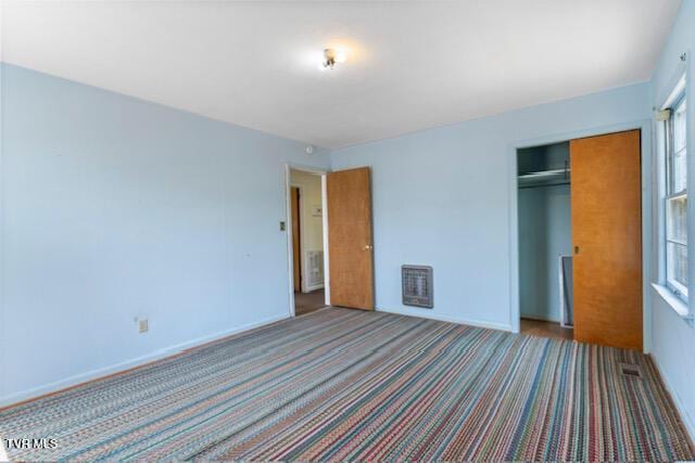 unfurnished bedroom with heating unit, carpet floors, baseboards, and a closet