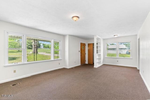 unfurnished living room featuring baseboards, visible vents, and dark colored carpet