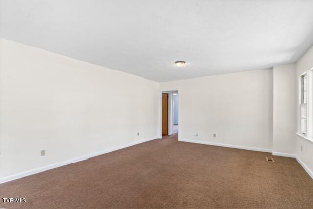 spare room with baseboards and dark colored carpet