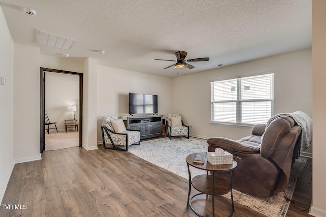 living area with a ceiling fan, a textured ceiling, visible vents, and wood finished floors
