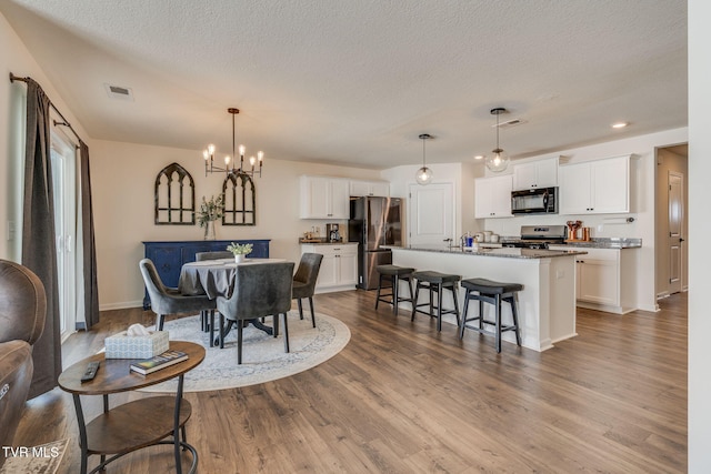 dining room with wood finished floors, a textured ceiling, a chandelier, and visible vents